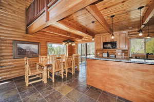 Kitchen featuring black microwave, beam ceiling, wooden ceiling, rustic walls, and dark stone countertops