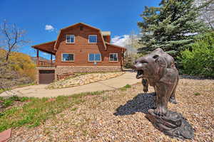 View of property exterior featuring a gambrel roof, an attached garage, log siding, driveway, and a balcony