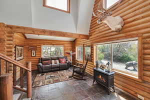Living room featuring a towering ceiling, a wood stove, rustic walls, stairway, and dark stone finish flooring