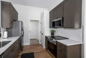 Kitchen featuring stainless steel appliances, decorative backsplash, light countertops, light wood finished floors, and baseboards