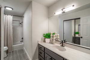 Bathroom featuring toilet, shower / tub combo with curtain, vanity, tile patterned flooring, and baseboards