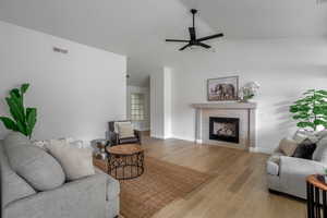 Living room with ceiling fan, a fireplace, lofted ceiling, light wood finished floors, and baseboards