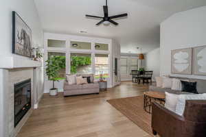 Living room with lofted ceiling, a fireplace, ceiling fan, light wood finished floors, and baseboards