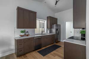 Kitchen with appliances with stainless steel finishes, a sink, backsplash, light countertops, and high vaulted ceiling