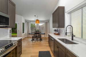 Kitchen featuring appliances with stainless steel finishes, a sink, backsplash, and dark brown cabinetry