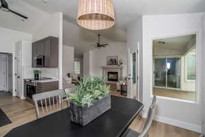 Dining space with lofted ceiling, a ceiling fan, light wood-style floors, baseboards, and a fireplace