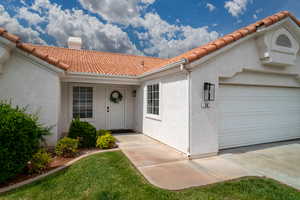 Doorway to property featuring a tiled roof, a chimney, stucco siding, and a garage