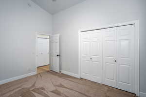Unfurnished bedroom with carpet floors, high vaulted ceiling, and baseboards