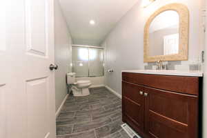 Bathroom featuring bath / shower combo with glass door, vanity, toilet, baseboards, and wood tiled floors