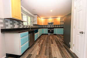 Kitchen featuring stainless steel appliances, open shelves, dark countertops, dark wood-style flooring, and decorative backsplash