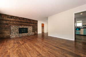 Unfurnished living room featuring dark wood-style floors, a large fireplace, and baseboards