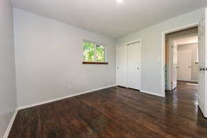 Unfurnished bedroom featuring baseboards, dark wood-style flooring, and a closet