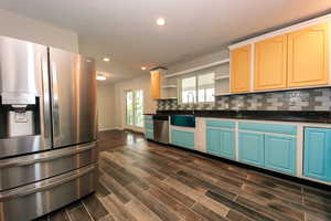 Kitchen featuring appliances with stainless steel finishes, a sink, open shelves, dark countertops, and recessed lighting