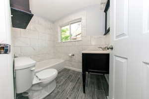 Full bath featuring tile walls, toilet, vanity, a tub to relax in, and wood finish floors