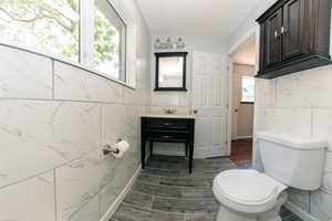 Bathroom featuring tile walls, vanity, toilet, and wood finished floors