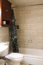 Bathroom with toilet, tile walls, and shower / bath combo with shower curtain