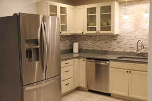 Kitchen featuring appliances with stainless steel finishes, a sink, backsplash, light tile patterned floors, and dark stone counters