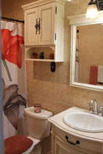 Bathroom with vanity, tile walls, decorative backsplash, a shower with shower curtain, and toilet