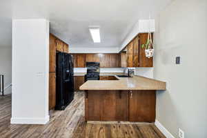 Kitchen with black appliances, a peninsula, baseboards, light countertops, and wood finished floors