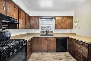 Kitchen featuring black appliances, a sink, under cabinet range hood, light wood finished floors, and light countertops