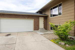 Property entrance with driveway, brick siding, a garage, and a shingled roof