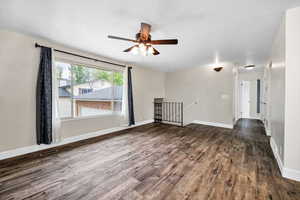 Empty room featuring dark wood-type flooring, a ceiling fan, and baseboards