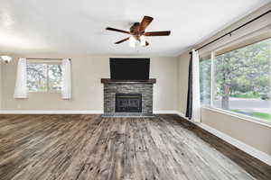 Unfurnished living room with wood finished floors, a ceiling fan, a fireplace, and baseboards