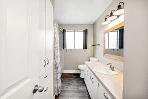 Bathroom with wood finished floors, toilet, vanity, baseboards, and a shower with shower curtain