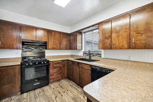 Kitchen featuring black appliances, a sink, light wood-style flooring, light countertops, and dark brown cabinets