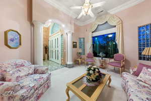 Carpeted living room featuring ornate columns, ornamental molding, and ceiling fan