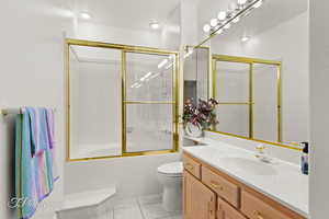 Full bathroom with tile patterned floors, vanity, toilet, and combined bath / shower with glass door