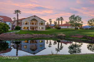 Back of property at dusk featuring a balcony, a yard, and a water view
