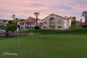 Rear view of house with a balcony, an area to practice putting, a yard, and a chimney
