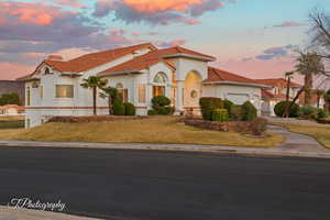 Mediterranean / spanish-style house featuring a garage, a tiled roof, stucco siding, a lawn, and a chimney