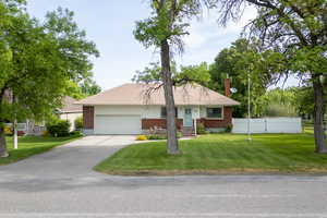 Single story home with brick siding, an attached garage, driveway, and a chimney