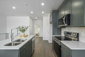 Kitchen featuring stainless steel appliances, a sink, decorative backsplash, dark wood finished floors, and light countertops