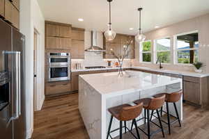 Kitchen with stainless steel appliances, wall chimney range hood, a sink, dark wood finished floors, and a kitchen island