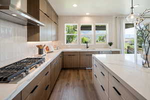 Kitchen with wall chimney range hood, a sink, stainless steel gas stovetop, backsplash, and recessed lighting