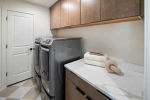 Clothes washing area featuring cabinet space, washer and clothes dryer, and light floors