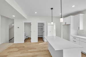 Kitchen featuring light wood finished floors, light countertops, white cabinets, recessed lighting, and a grey center island