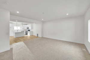 Living room with light colored carpet, baseboards, a sink, recessed lighting, and light wood-style flooring