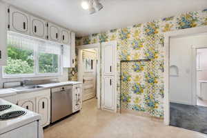 Kitchen with stainless steel dishwasher, a sink, wallpapered walls, light countertops, and white cabinets