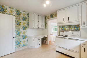 Kitchen with range with two ovens, wallpapered walls, light countertops, and baseboards