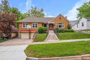 View of front of house featuring brick siding, driveway, a front lawn, an attached garage, and a chimney