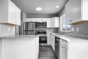 Kitchen with appliances with stainless steel finishes, a sink, a textured ceiling, white cabinetry, and light granite counters