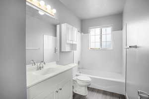 Full bath featuring LVP wood look finished floors, a textured ceiling, vanity, toilet, and bathtub / shower combination