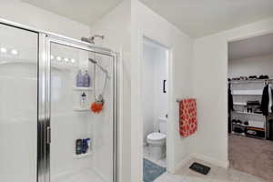 Bathroom with a stall shower, tile patterned floors, toilet, baseboards, and a spacious closet