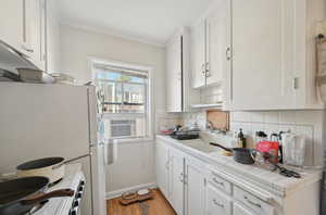 Kitchen featuring white cabinets, tasteful backsplash, light wood-style floors, tile counters, and white appliances