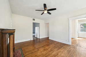Unfurnished living room featuring a ceiling fan, dark wood-type flooring, and baseboards