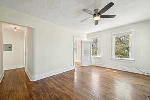 Unfurnished room featuring ceiling fan, hardwood / wood-style floors, baseboards, a textured ceiling, and electric panel